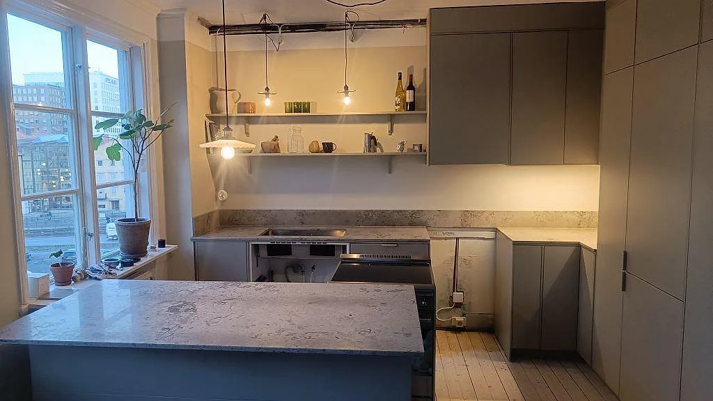 Köksbänkskiva och halvö i matt Jura Grey kalksten i ett kök med mörka luckor och stort fönster i Göteborg.