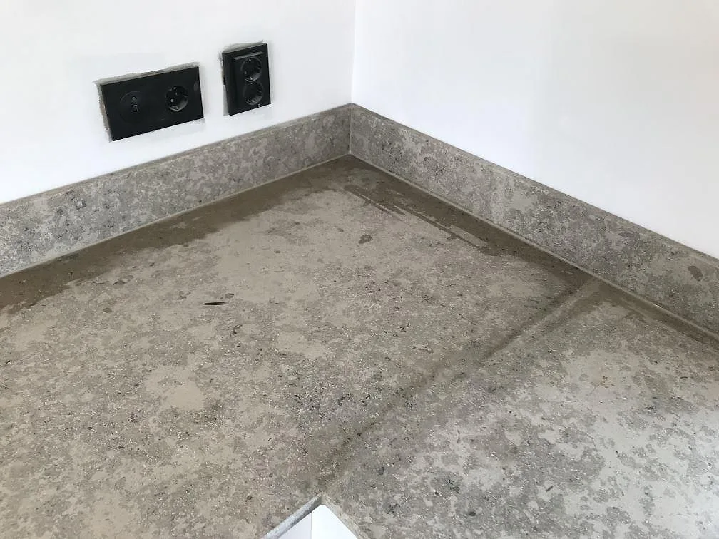 Hörn av köksbänkskiva i matt Jura Grey kalksten med låg uppvikt stänkkant och eluttag, kök i Häljarp.