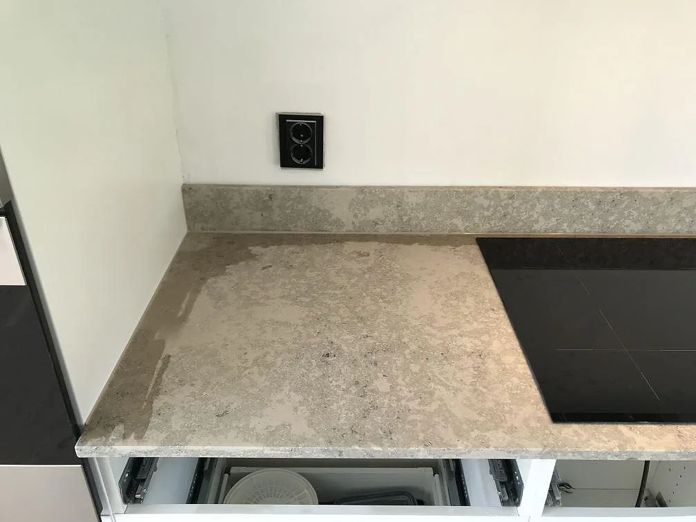 Köksbänkskiva i matt Jura Grey kalksten i Häljarp med uppvikt stänkkant och infälld Smeg-induktionshäll längs väggen.