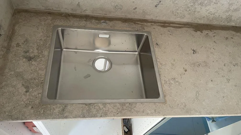 Rostfri diskho i en köksbänkskiva av matt Jura Grey, med kalkstensyta och stänkskydd i Hindås.