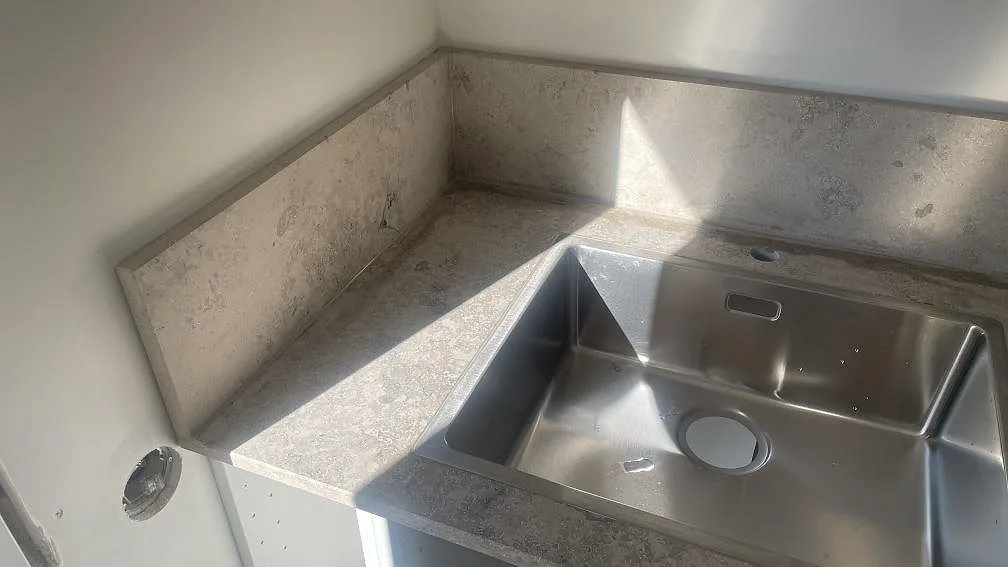 Detalj av matt Jura Grey runt rostfri diskho och uppvikt stänkskydd, fotograferad under montering i Hindås.