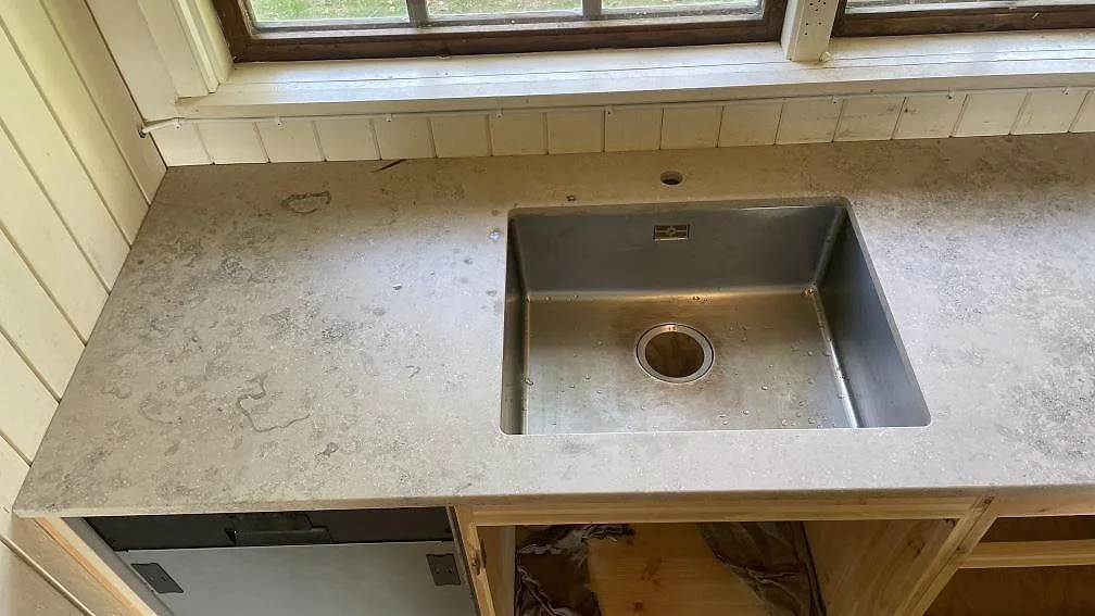 Närbild på matt Jura Grey köksbänkskiva i kalksten med synlig rostfri diskho vid fönster i ett kök i Höör.