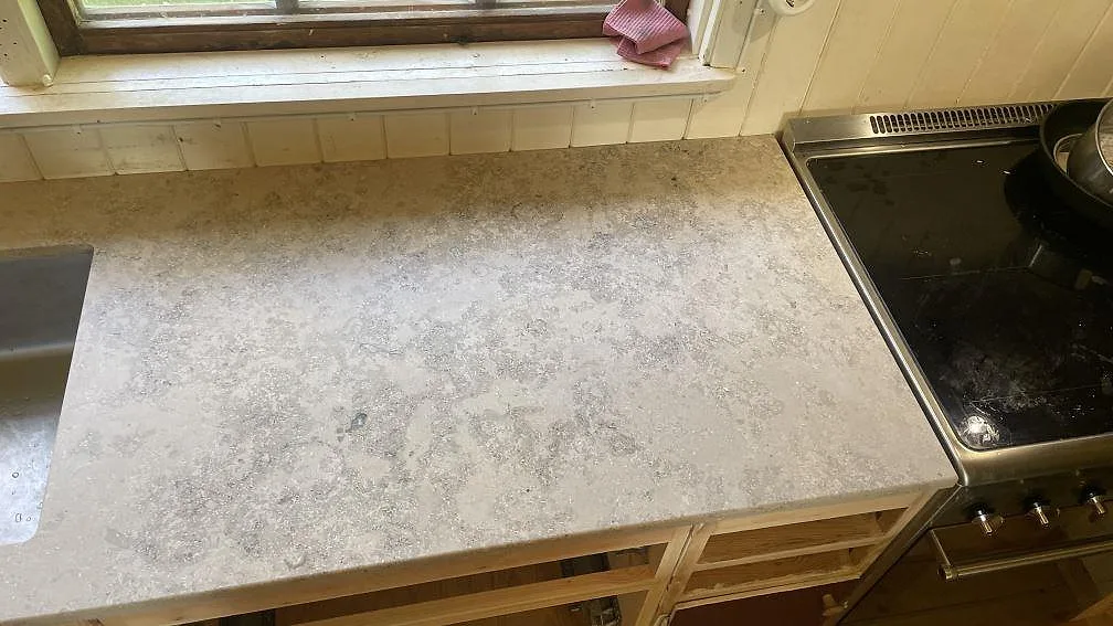 Matt Jura Grey kalksten på köksbänk mellan diskho och spis, med gråbeige fossilstruktur i ett kök i Höör.