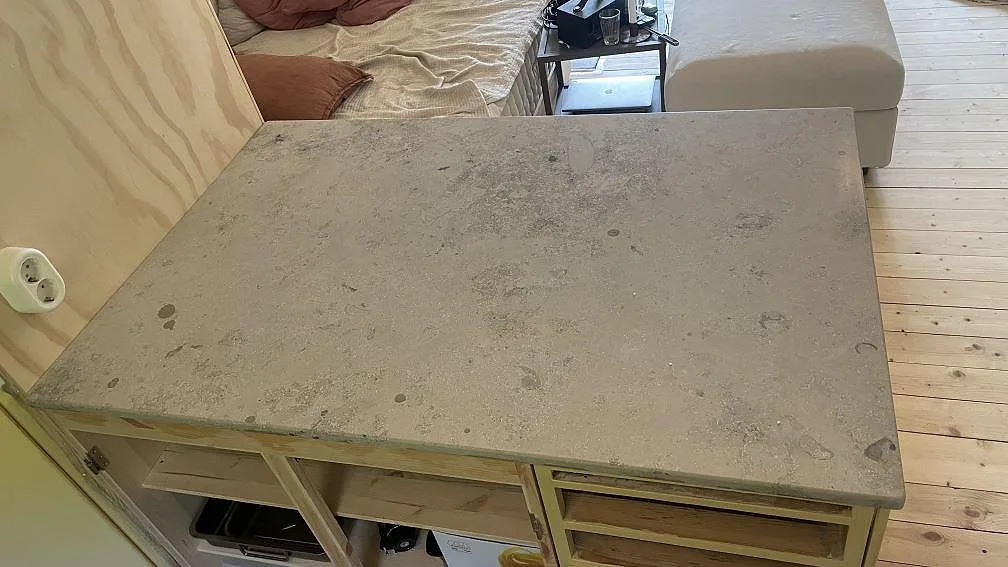 Separat köksö med bänkskiva i matt Jura Grey kalksten, fossilrik gråbeige yta och trästommar i ett kök i Höör.