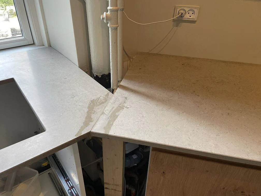 Närbild av innerhörn i matt Jura Grey där bänkskivan möter fönstersidan och rördragningen i köket i København.