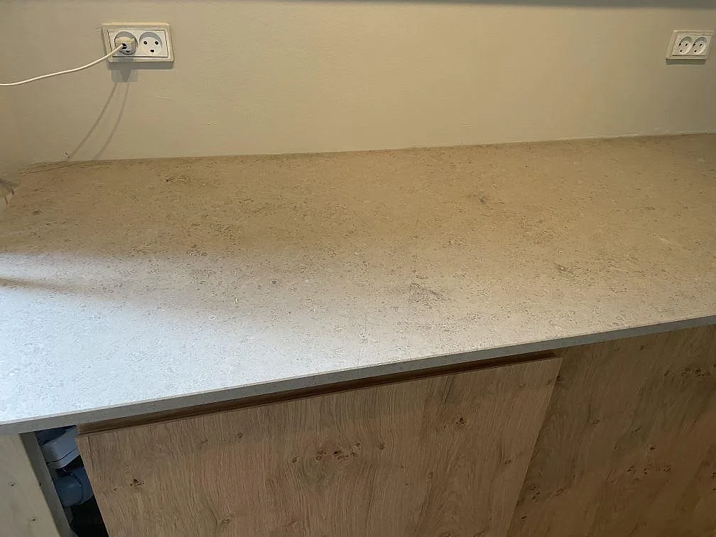Rak arbetsyta i matt Jura Grey kalksten över träinredning och vägguttag i köket i København.