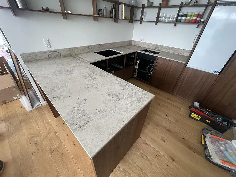 Köksbänkskiva i Jura Grey kalksten, matt 20 mm, i U-format med valnötsstommar och induktionshäll på plats i ett kök i København.