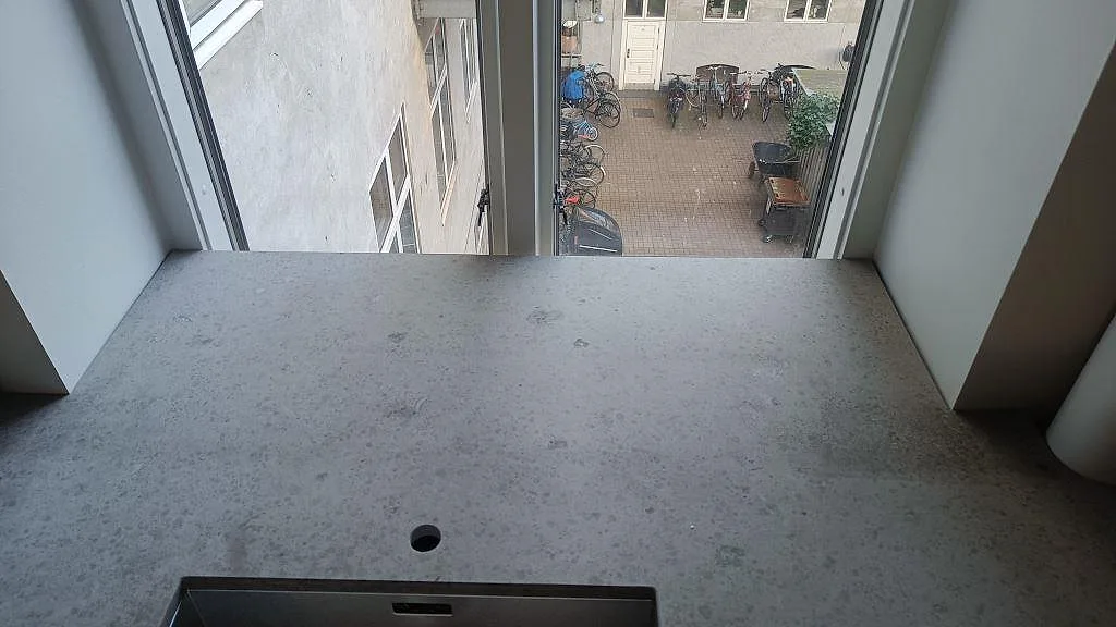 Toppvy över monterad Jura Grey köksbänkskiva med blandarhål och underlimmad diskho framför fönster i København N.