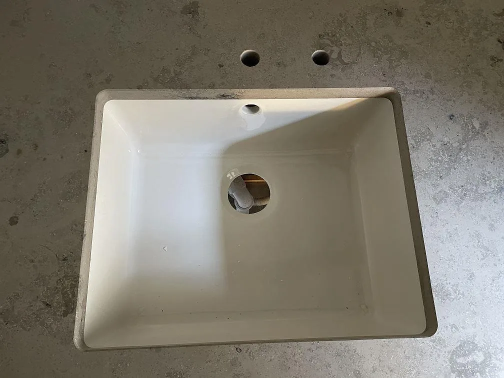 Vit diskho ovanpå matt Jura Grey kalksten med kranhål i ett kök i København N.