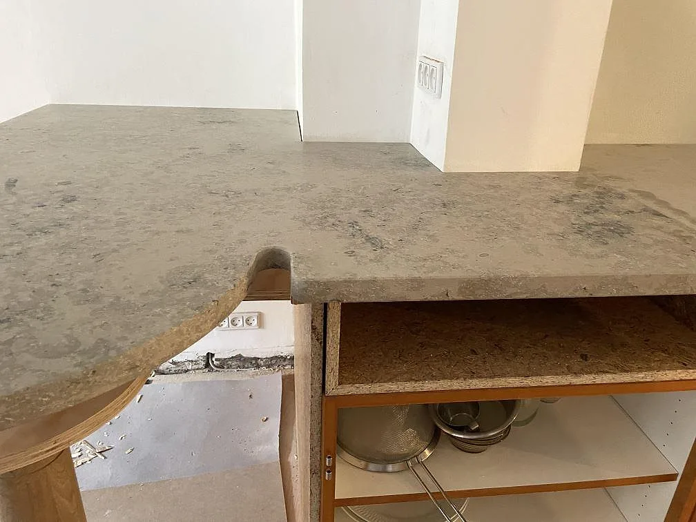 L-formad köksbänkskiva i matt Jura Grey kalksten med rundad peninsula och öppen träinredning i København N.
