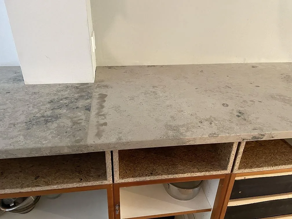 Rak bänkyta i matt Jura Grey kalksten över öppna trästommar i ett kök i København N.