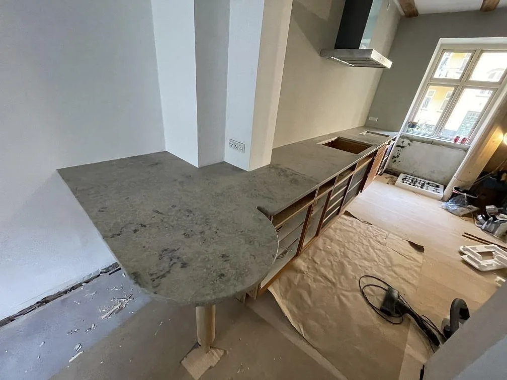Köksbänkskiva i matt Jura Grey kalksten med rundad halvö, hällöppning och stenklädd fläktkåpa i ett kök i København N.
