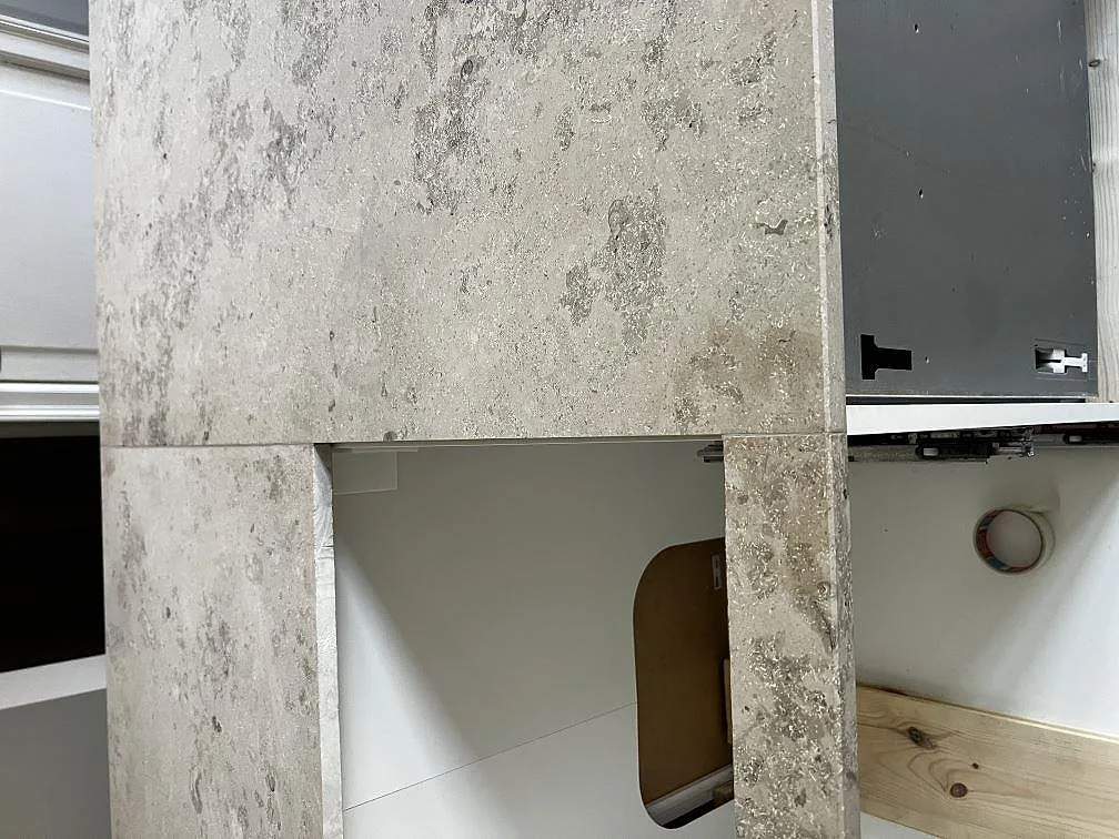 Köksö i Jura Grey kalksten med nedvikt gavel och synlig fossilstruktur, matt yta, i ett kök under montering i København Ø.