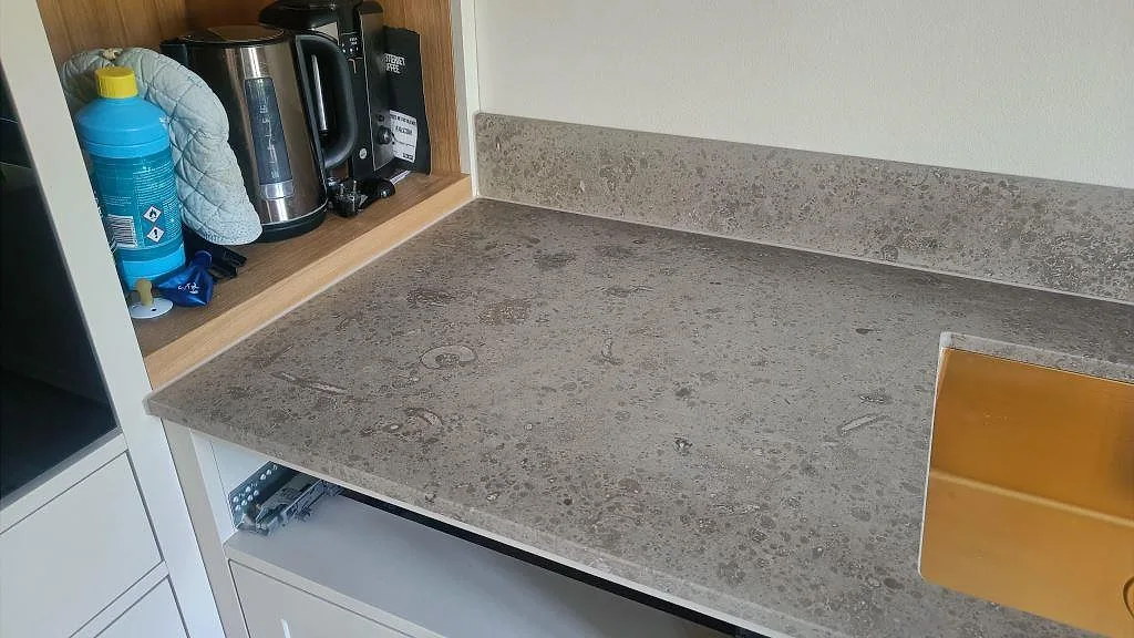 Sinkdel i matt Jura Grey kalksten med uppvikt stänkkant och guldfärgad diskho under montering i Köpenhamn.