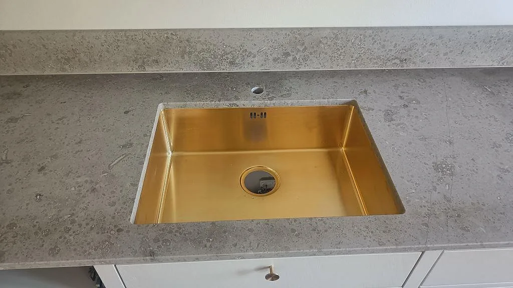 Matt Jura Grey kalksten med guldfärgad underlimmad diskho, tapphål och låg stänkkant i ett kök i Köpenhamn.