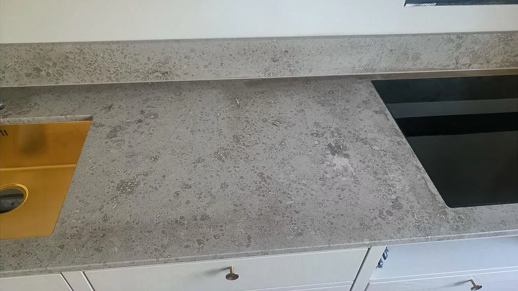 Köksbänkskiva i matt Jura Grey kalksten med guldfärgad diskho och svart induktionshäll under montering i Köpenhamn.
