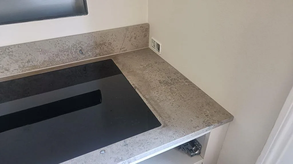 Detalj av matt Jura Grey kalksten vid svart häll och hörn med låg stänkkant i ett kök i Köpenhamn.