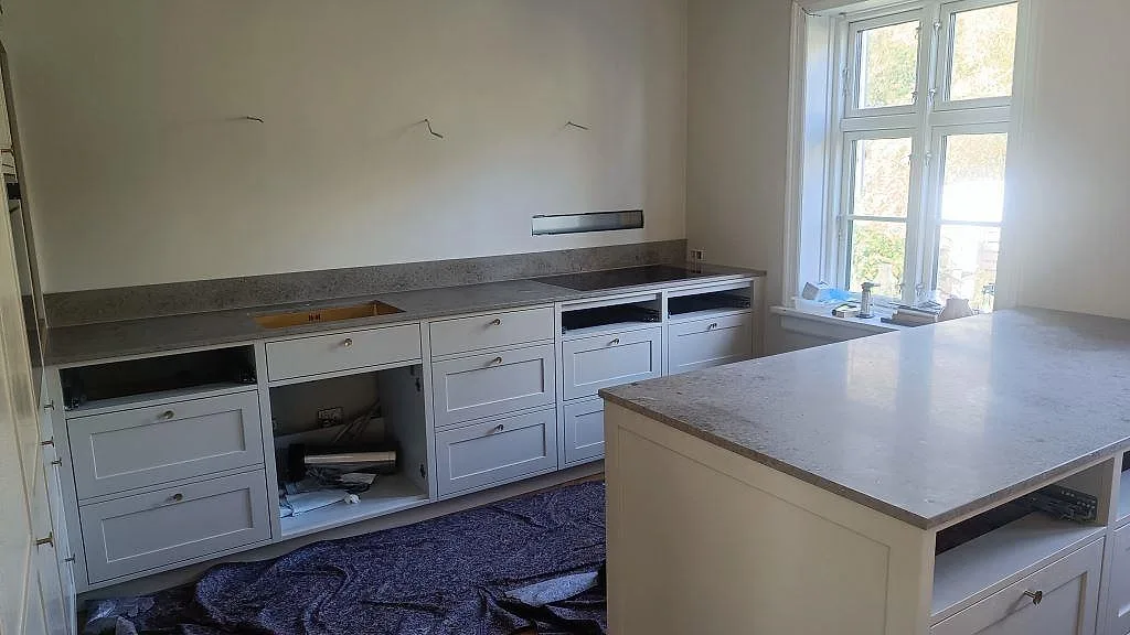 Köksbänkskiva i 20 mm matt Jura Grey kalksten med halvö, vit köksinredning och fönster i Köpenhamn.