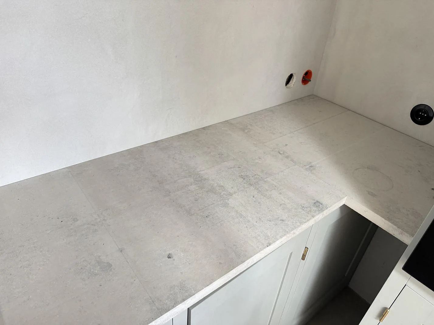 Hörndel av köksbänkskiva i matt Jura Grey kalksten med ljus ådring och eluttag i väggen under montering i Köpenhamn.