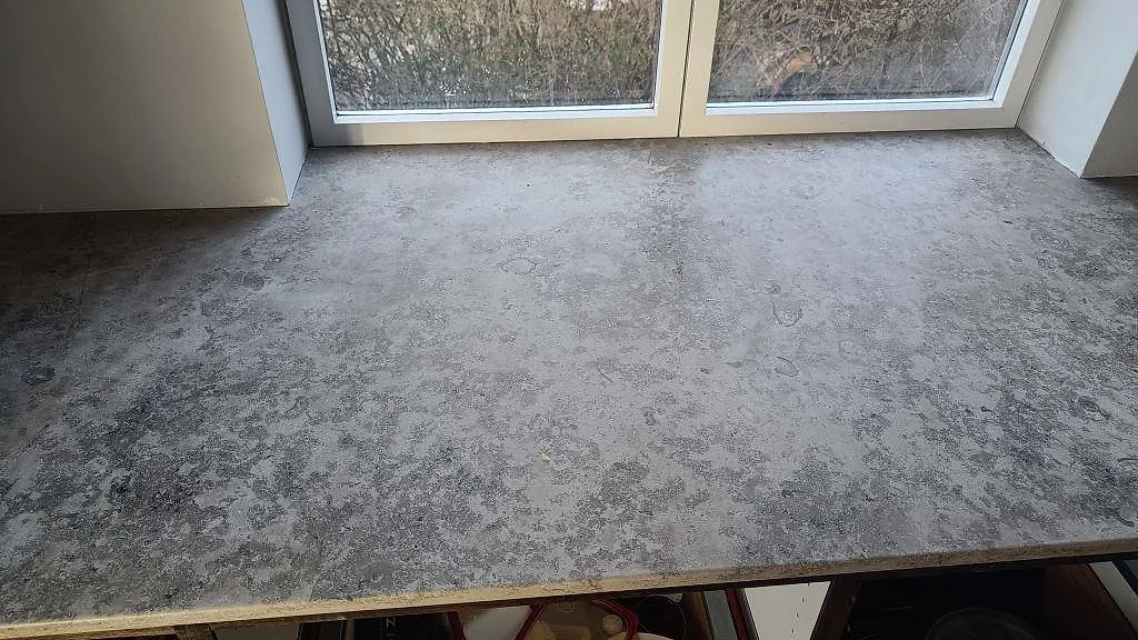 Ovanifrån av köksöns hörn i matt Jura Grey kalksten med tydliga fossilavtryck i ett kök i Kongens Lyngby.