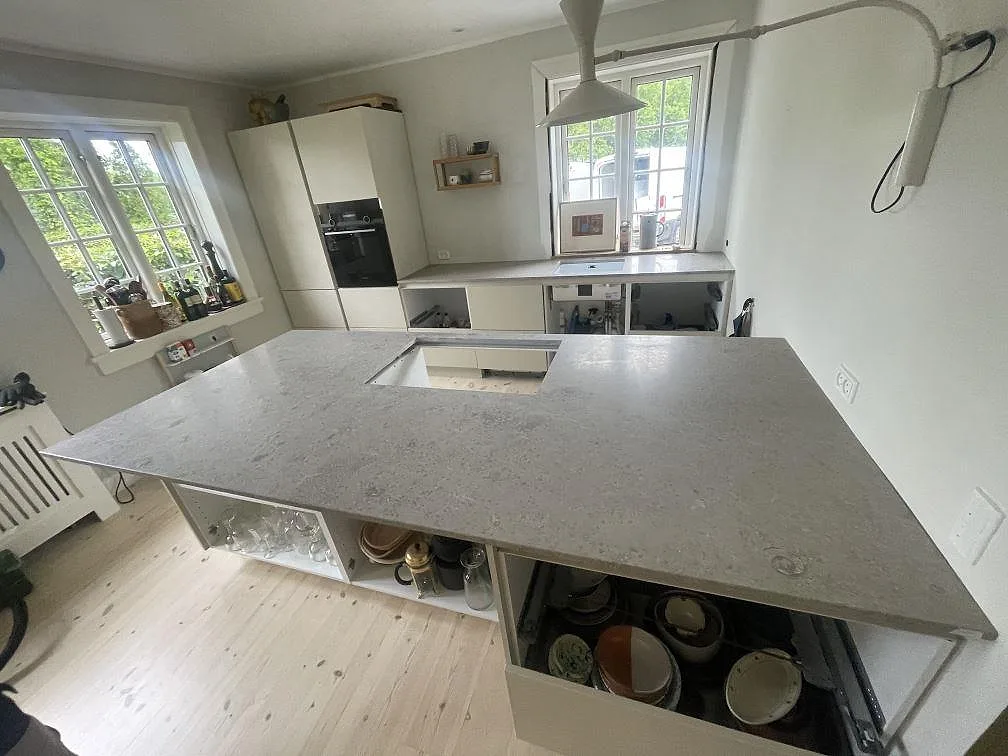 Stor köksö med köksbänkskiva i Jura Grey kalksten, matt finish och urtag för häll i ett ljust kök i Kongens Lyngby.