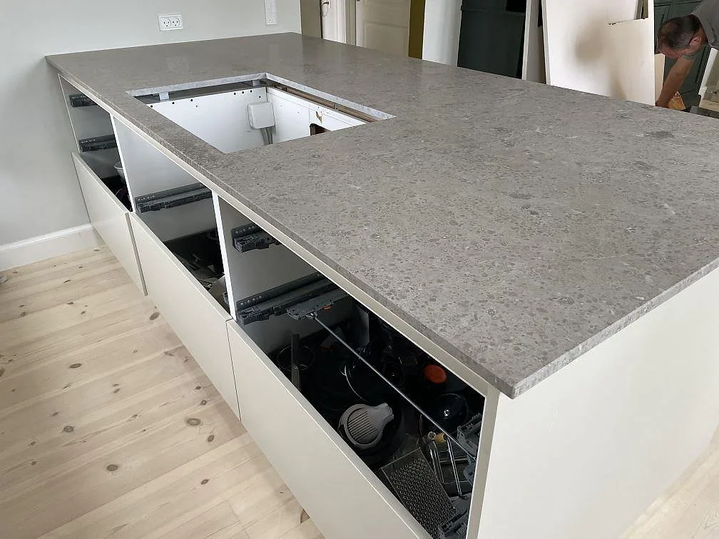 Köksö med bänkskiva i Jura Grey kalksten, matt yta och hällöppning under montering i ett kök i Kongens Lyngby.