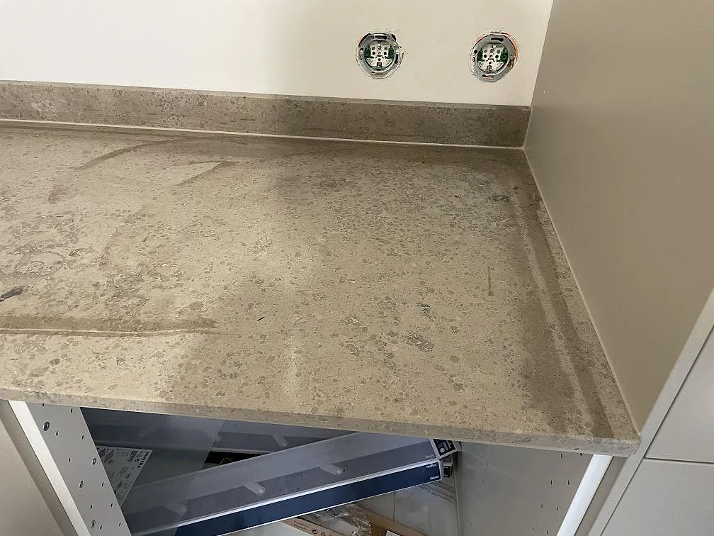 Hörnsektion i matt Jura Grey kalksten med stänkkant och öppna köksstommar under montering i Kortedala.