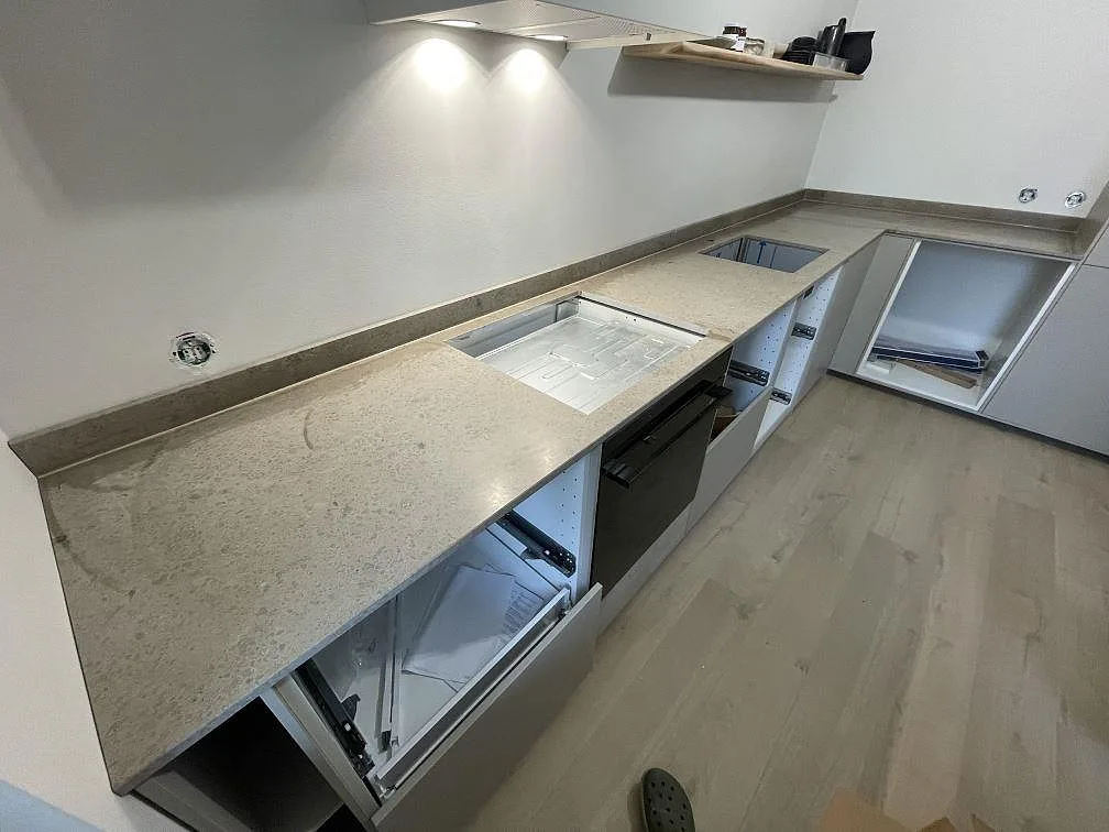 L-formad köksbänkskiva i matt Jura Grey kalksten med uppvikt stänkkant, hällurtag och underlimmad rostfri diskho i Kortedala.