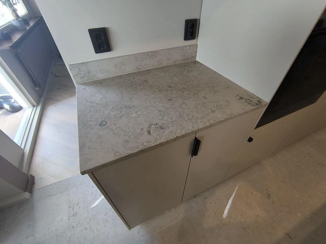 Detalj av matt Jura Grey kalksten på en sidobänk med uppvikt stänkkant och fossilrik yta i ett kök i Kungsängen.
