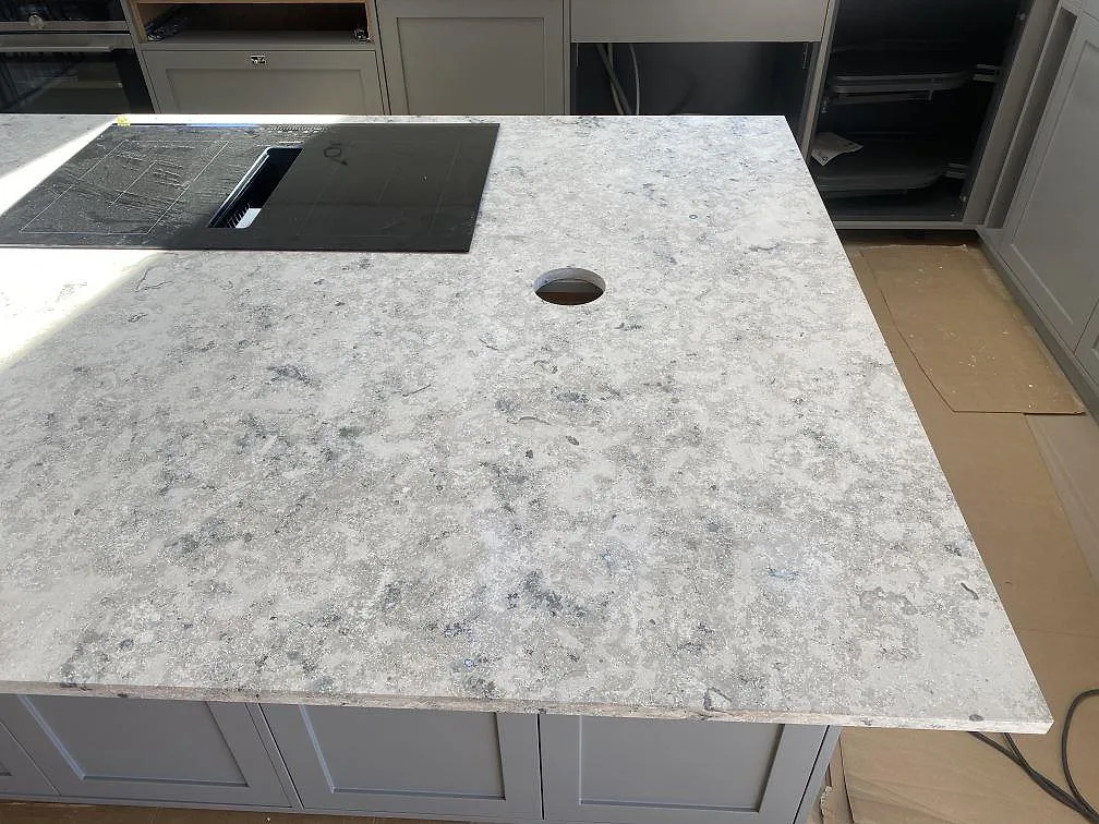 Köksbänkskiva i matt Jura Grey kalksten med svart induktionshäll på en halvö i ett kök i Kungshamn.