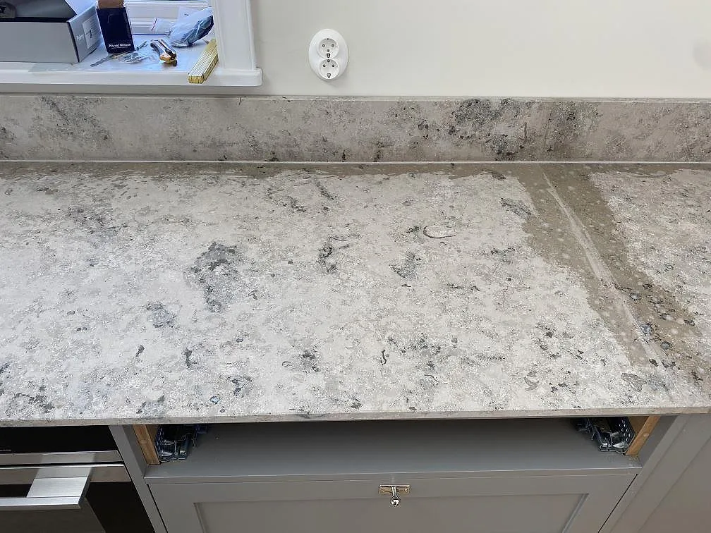 Installerad köksbänkskiva i matt Jura Grey kalksten med låg stänkkant och grågröna köksstommar i Kungshamn.