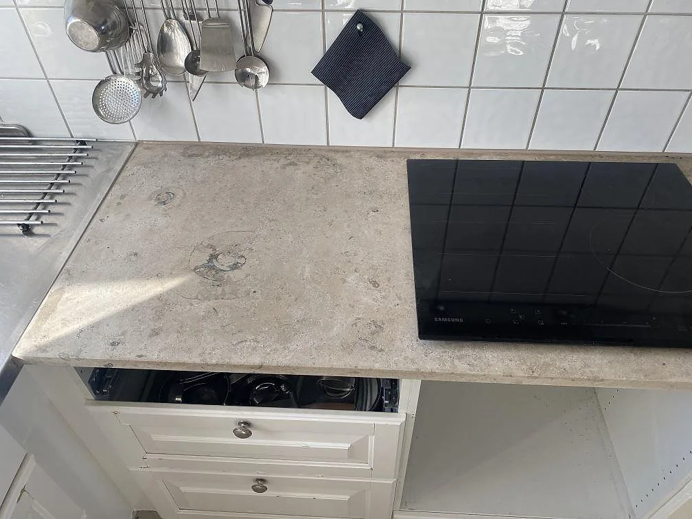 Infälld induktionshäll i en matt köksbänkskiva i Jura Grey kalksten med fossilmönster i Landskrona.