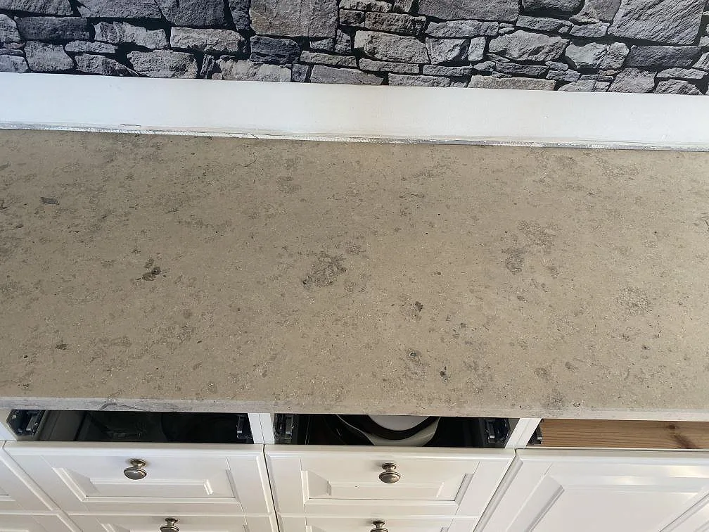 Bänkskiva i matt Jura Grey kalksten med naturlig fossilådring mot vägg i ett kök i Landskrona.