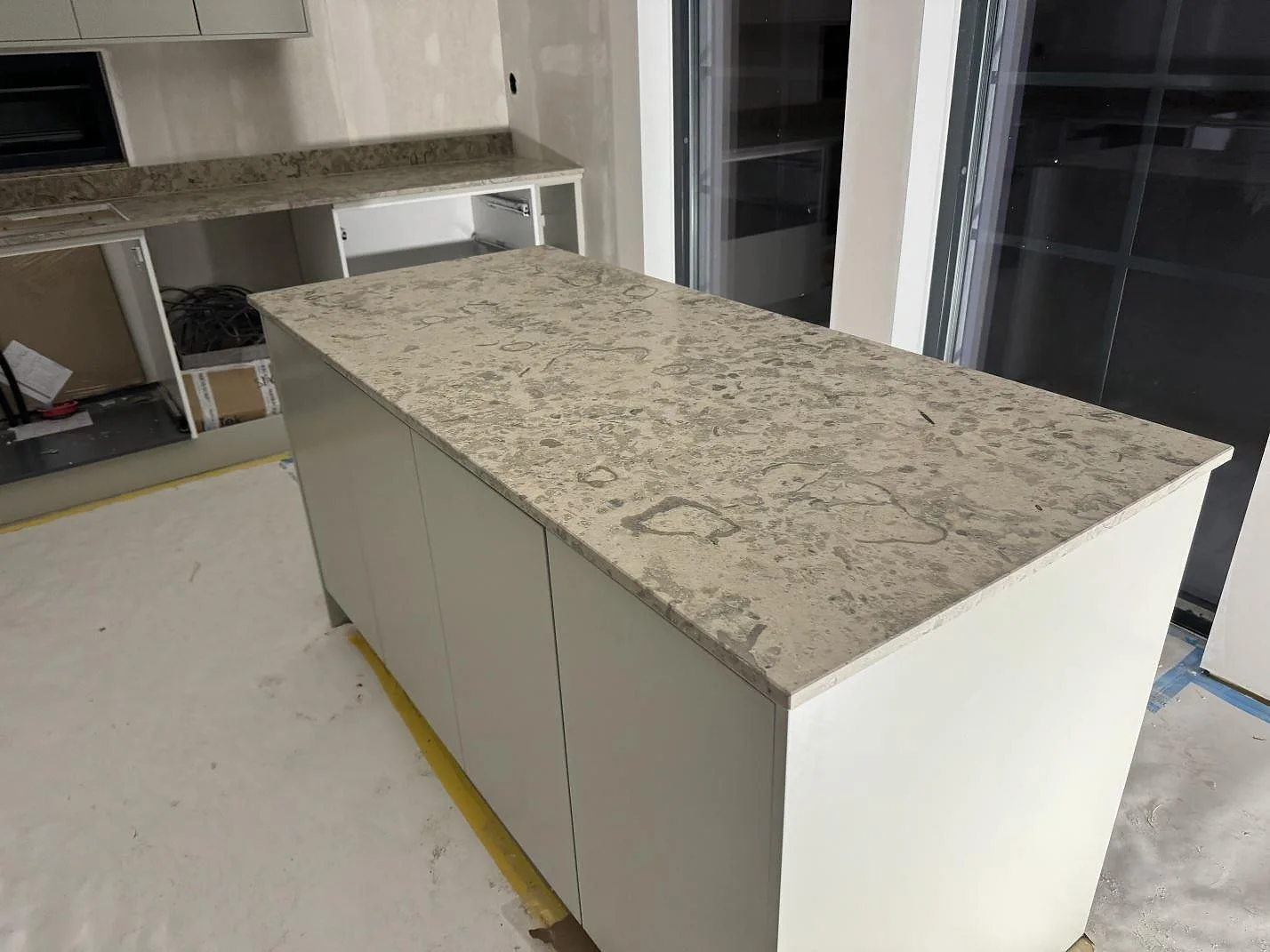 Fristående köksö med matt Jura Grey kalksten och stora fönster i ett kök under montering i Landvetter.