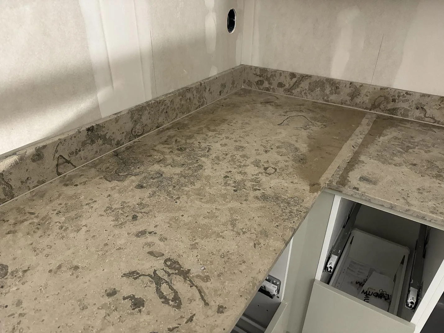 Hörnbänkskiva i matt Jura Grey kalksten med uppvikt stänkkant på vita köksstommar i Landvetter.