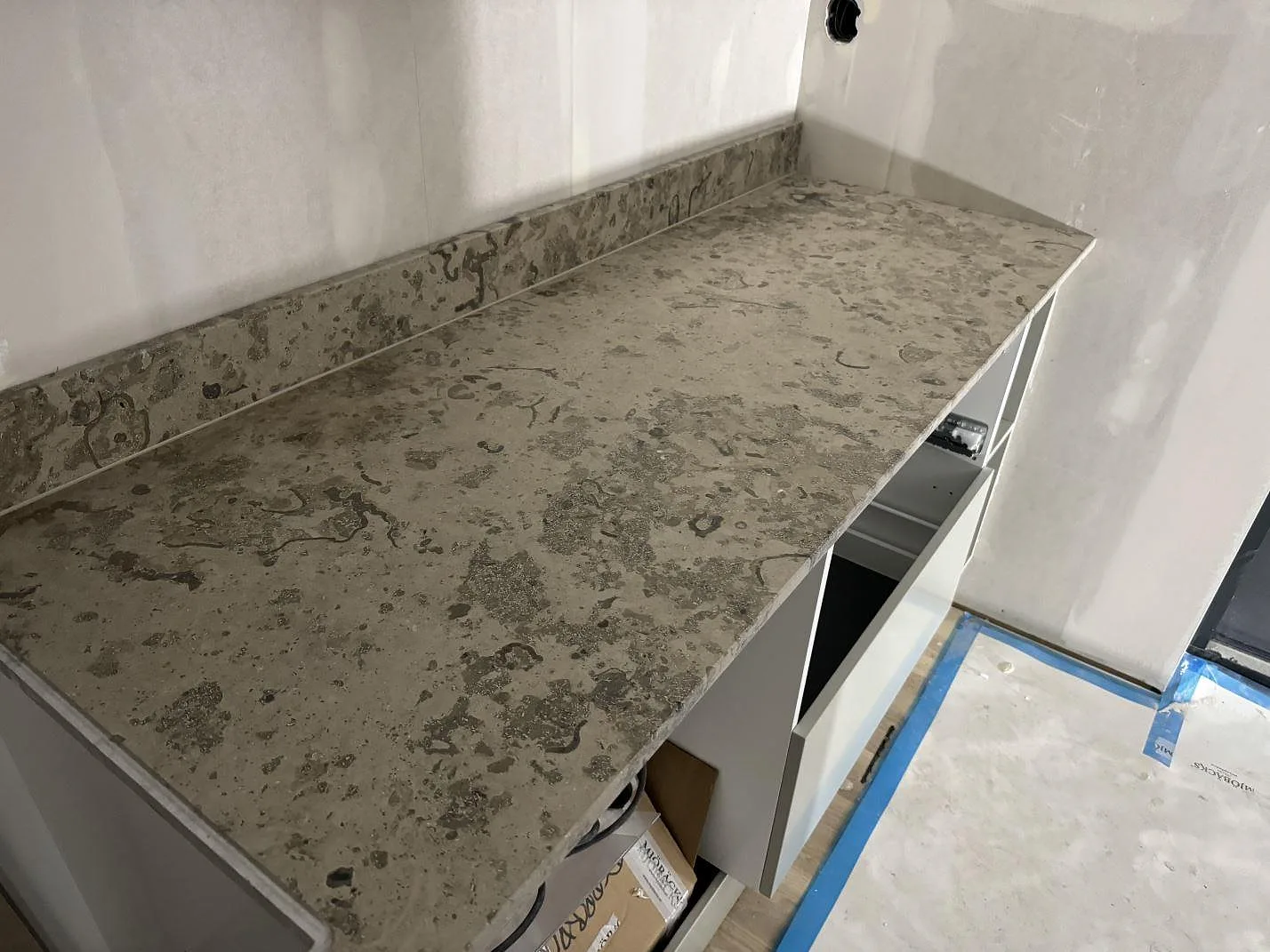 Lång köksbänk i Jura Grey kalksten, matt finish, med låg stänkkant vid stora fönster i Landvetter.