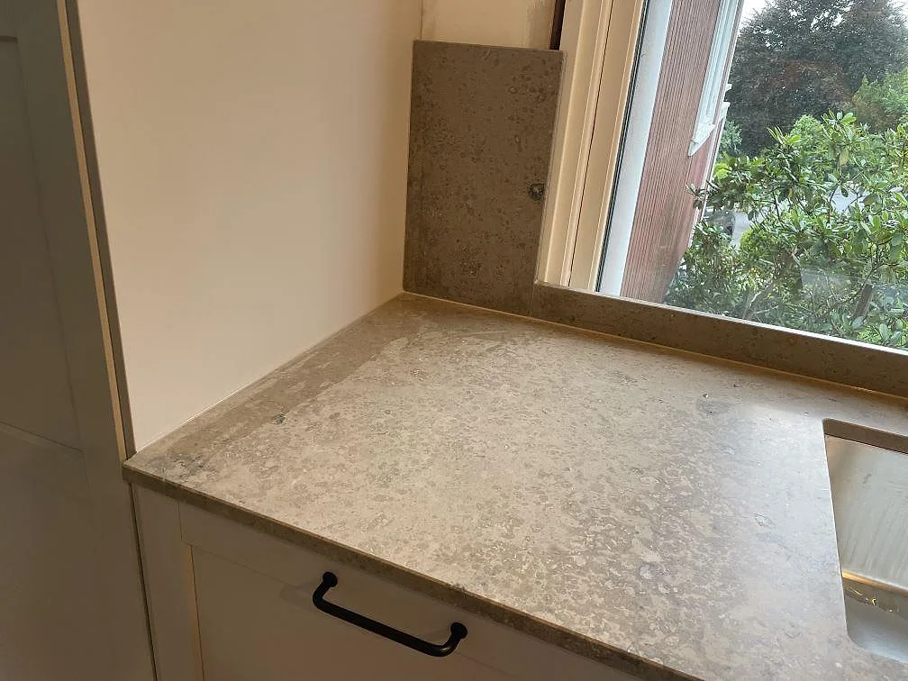 Matt Jura Grey kalksten som köksbänkskiva vid fönster med diskho och lodrätt stänkskydd i ett kök i Lekeryd.