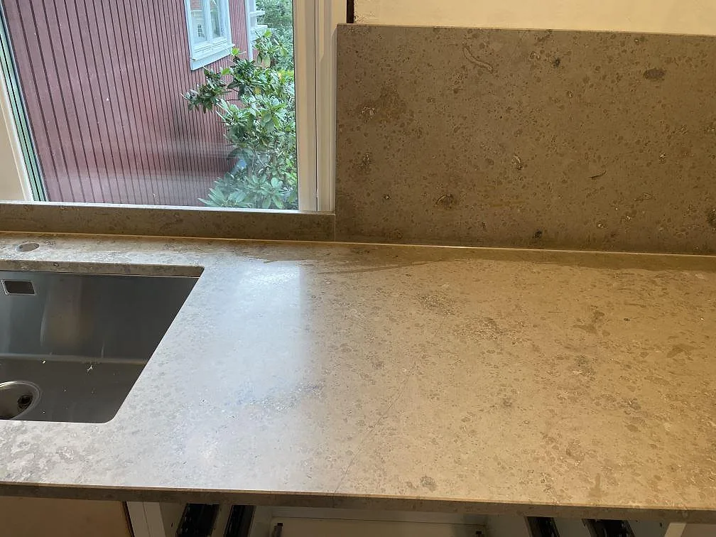 Köksbänkskiva i matt Jura Grey med rostfri diskho, låg stänkkant och högre stänkskydd vid fönster i Lekeryd.