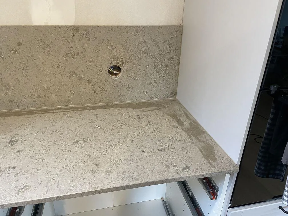 Höger del av köksbänkskiva i matt Jura Grey med stänkskydd, vägguttag och öppna stommar i Lekeryd.