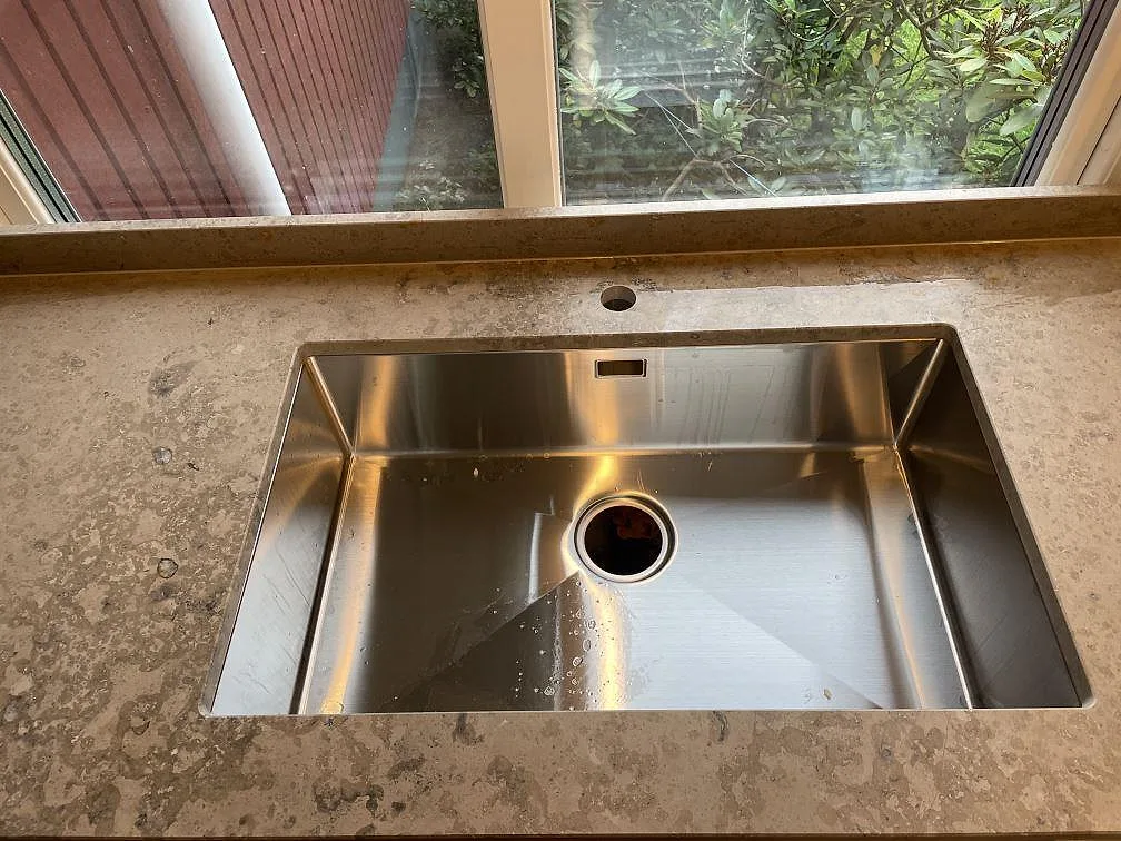 Närbild på underlimmad rostfri diskho i matt Jura Grey köksbänkskiva med stänkkant och fönster i Lekeryd.
