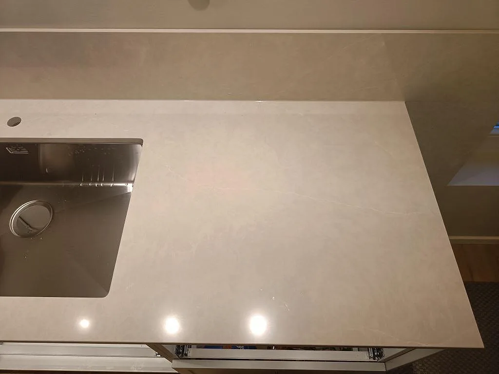 Detalj av matt Jura Grey bänkskiva med uppvikt stänkskydd och fossilådring vid fönstret i ett kök i Limhamn.