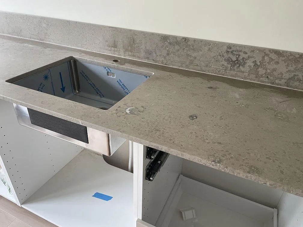 Underlimmad rostfri diskho i matt Jura Grey köksbänkskiva med stänkkant och vita köksstommar i Lindome.