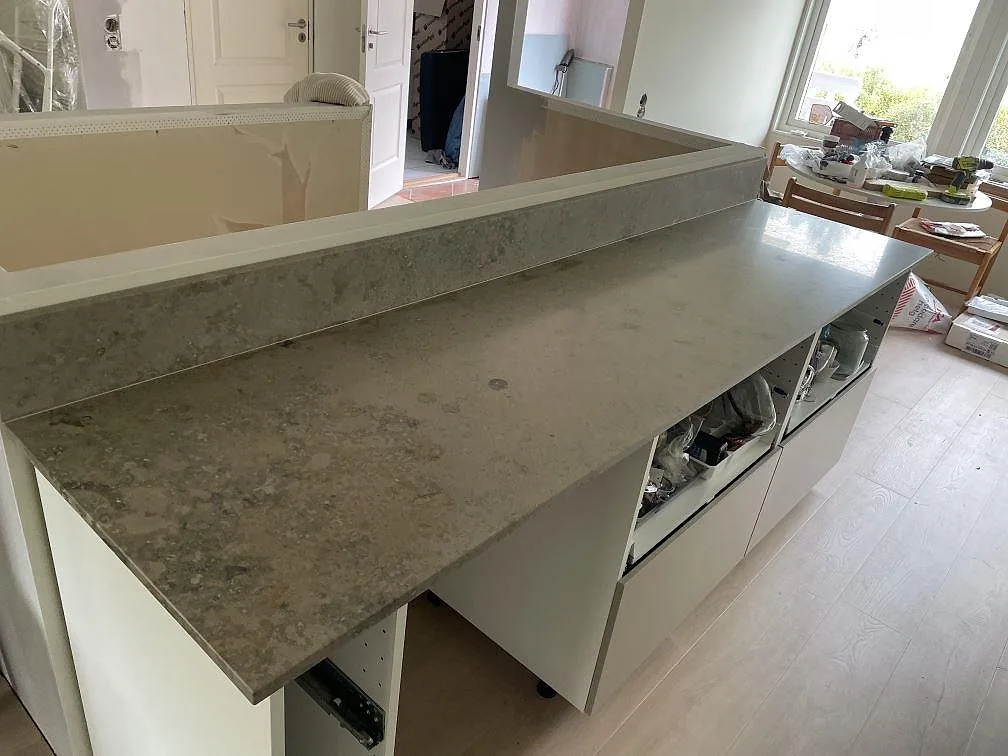 Köksbänkskiva i matt Jura Grey kalksten med lång bänkrad och uppvikt stänkkant i ett kök i Lindome.