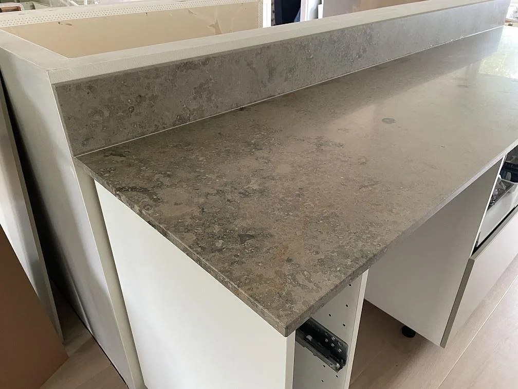 Närbild på matt Jura Grey kalksten som köksbänkskiva och stänkkant på vit halvö i Lindome.