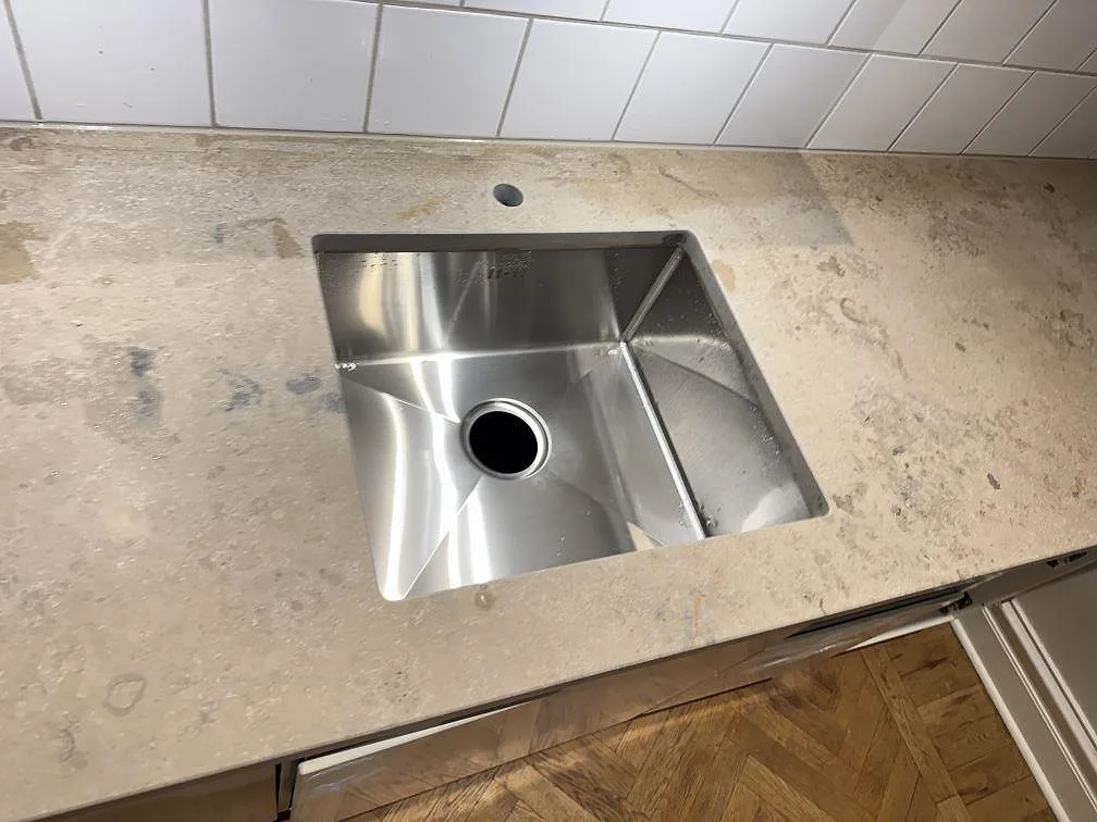 Diskhoområde i matt Jura Grey kalksten i Lund, där den gråbeige köksbänkskivan möter parkettgolv och vit kakelvägg.
