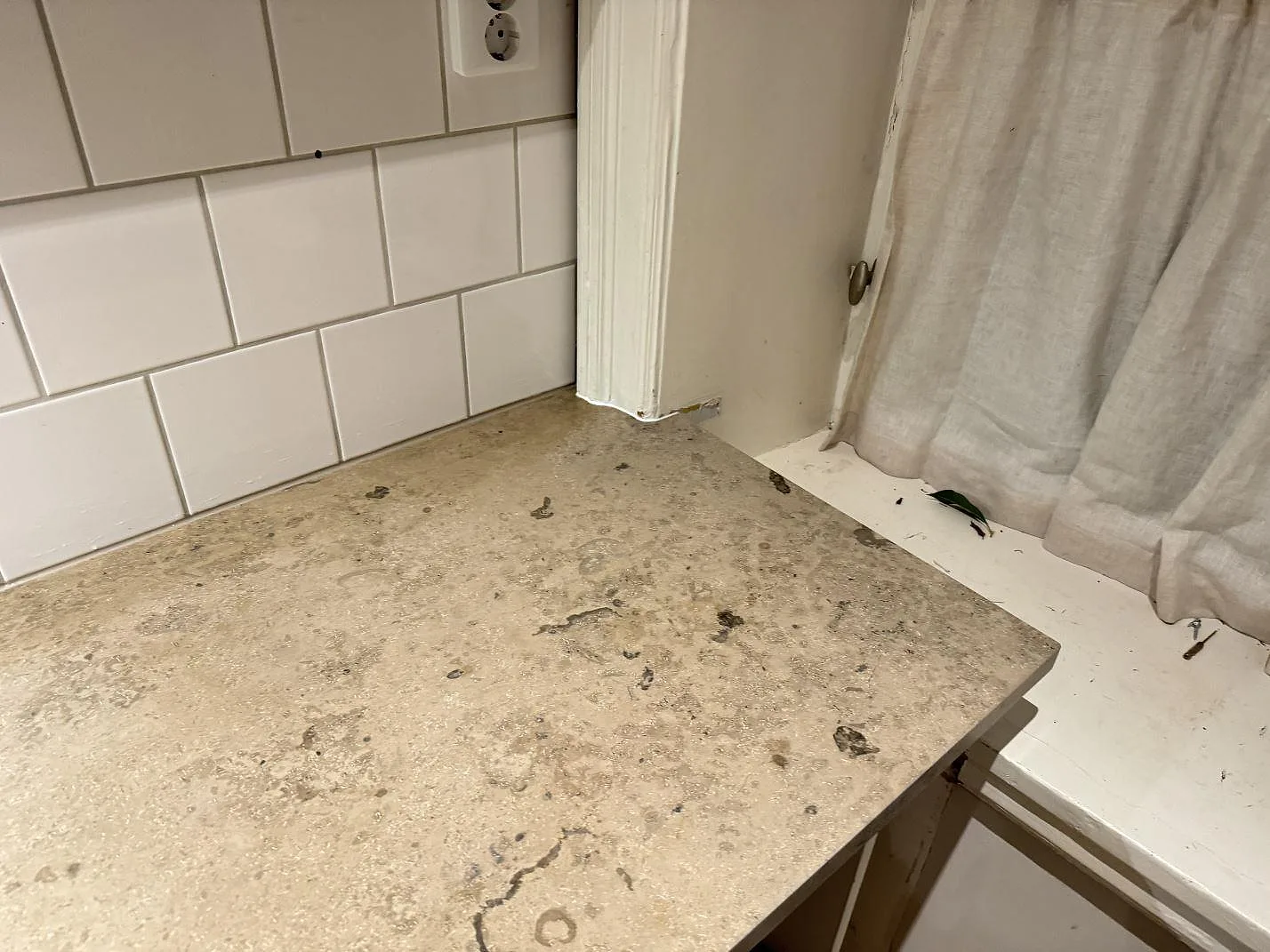 Hörn vid fönster med matt köksbänkskiva i Jura Grey kalksten i Lund, monterad mot vit kakelvägg och ljus köksinredning.