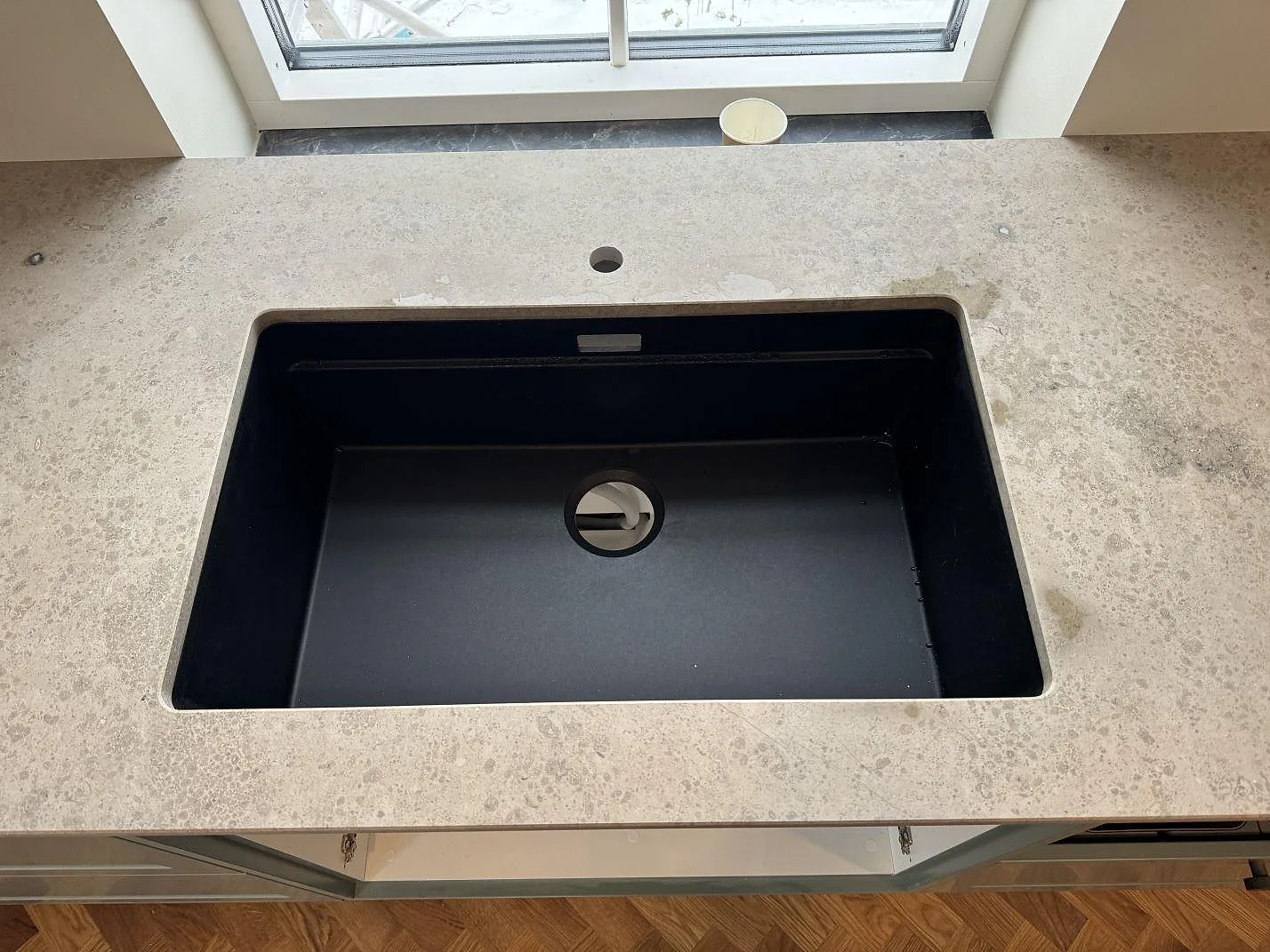 Närbild på svart ovanpåliggande diskho i matt Jura Grey kalksten framför fönster i Lyngby.
