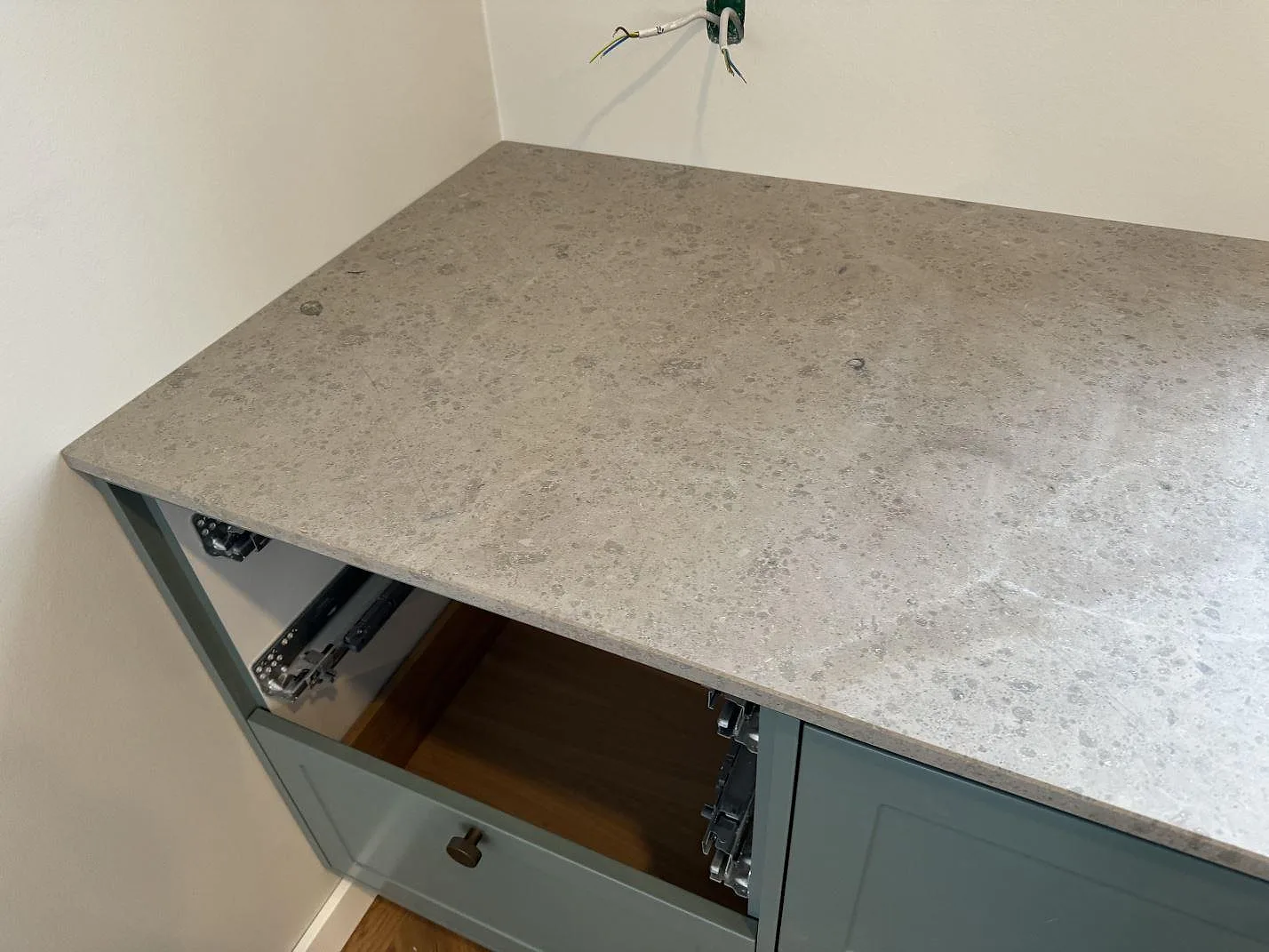 Hörnparti med köksbänkskiva i Jura Grey kalksten, matt, över grågröna stommar i Lyngby.