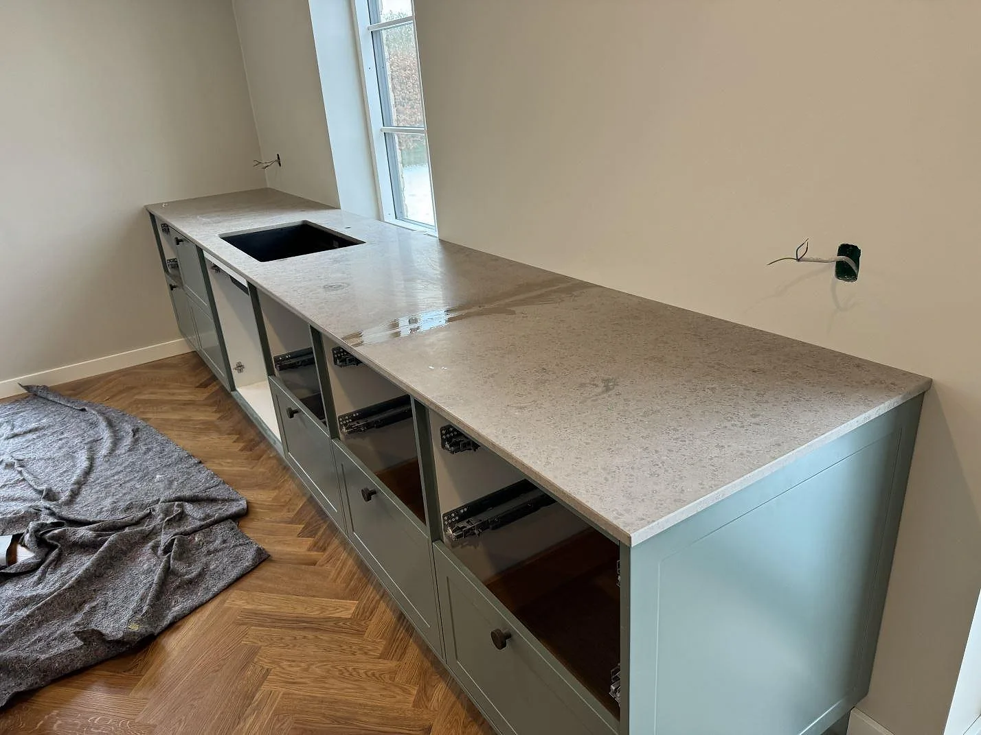 L-formad köksbänkskiva i matt Jura Grey med svart diskho och grågröna köksstommar i Lyngby.