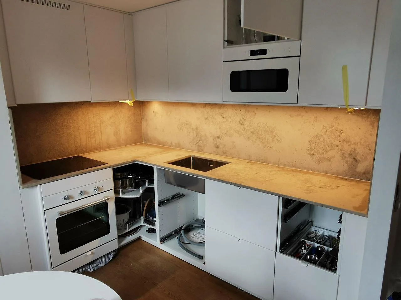 Köksbänkskiva i Jura Grey kalksten med matt yta, heltäckande stänkskydd, induktionshäll och underlimmad rostfri diskho i ett vitt greppfritt kök i Malmö.